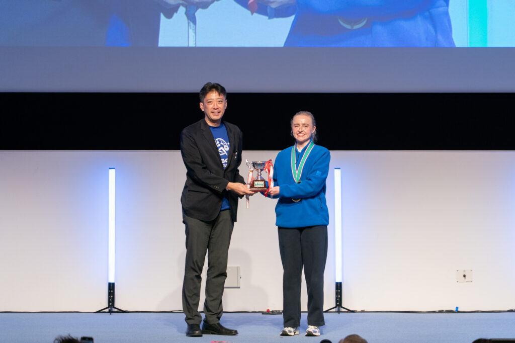 2023年大会優勝チーム英国のサラさんから優勝カップ返還